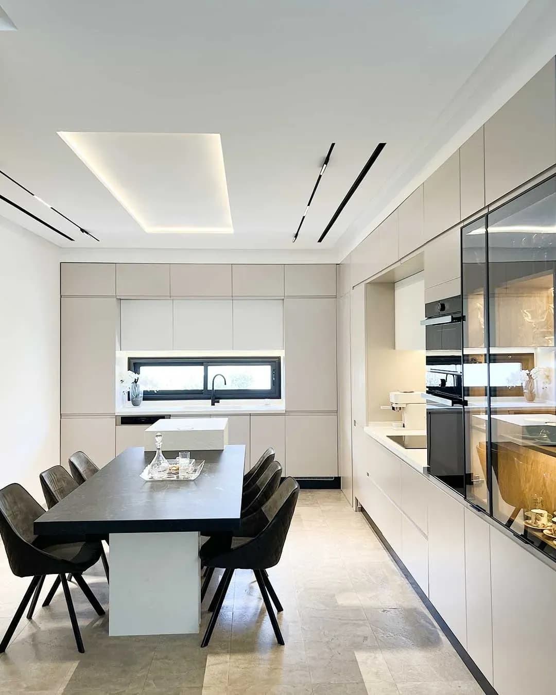 Cuisine Cuisina blanche contemporaine avec table centrale, rangements intégrés, électroménager encastré et vitrine éclairée.