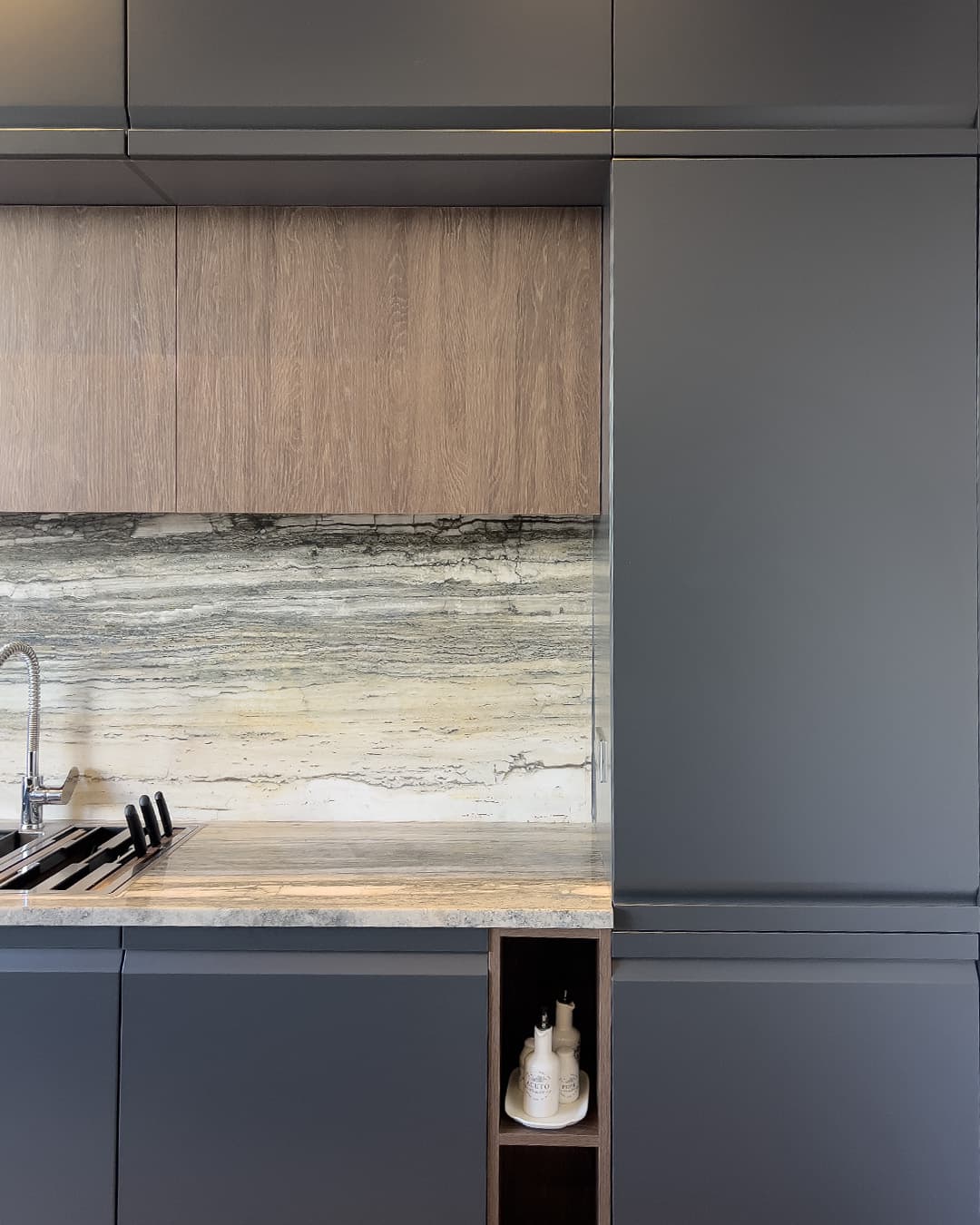 Cuisine Cuisina contemporaine avec façades bleu nuit, éléments en bois, crédence effet pierre et niche décorative intégrée.